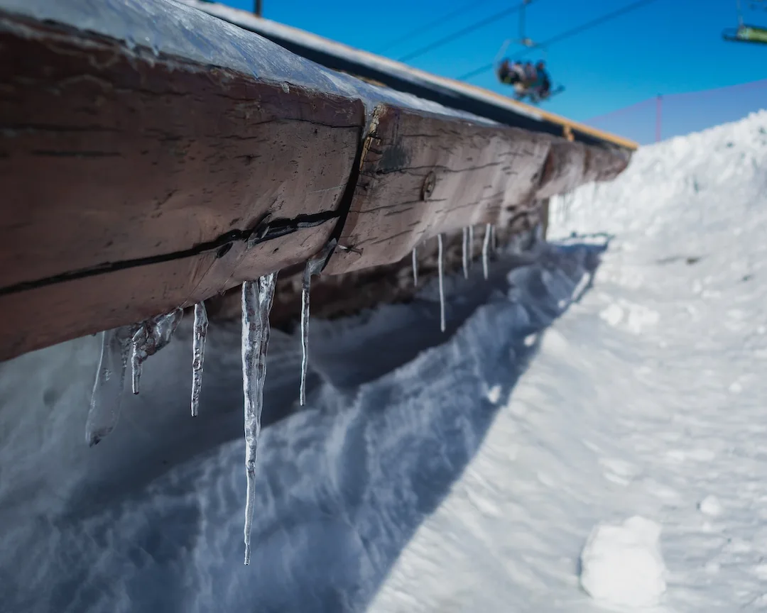 ice dam on wooden edge with icicles and blurry ski lift in snowy background