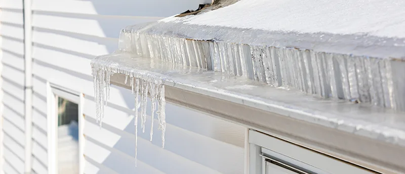 icicles hanging from snowy roof edge above window on white siding