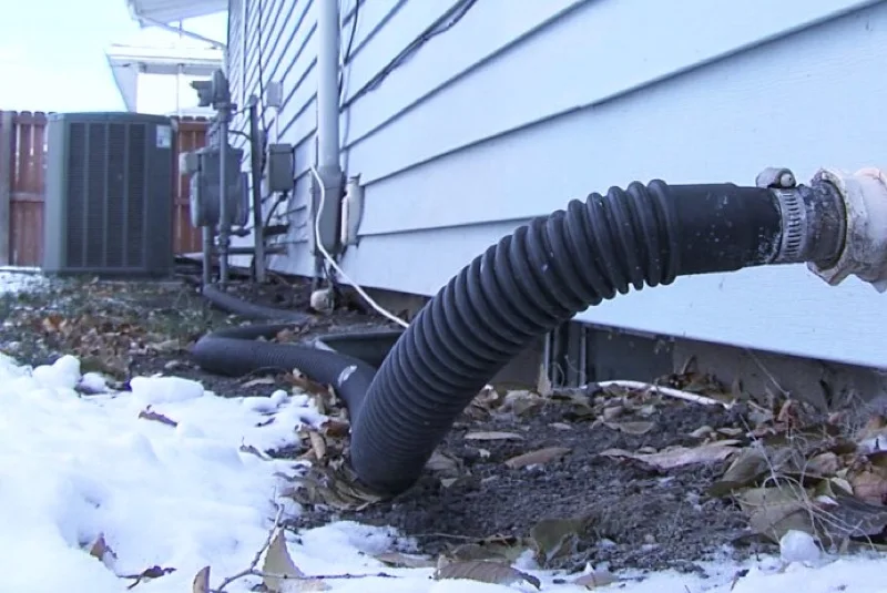 sump pump discharge hose disconnected lying on snowy ground by foundation